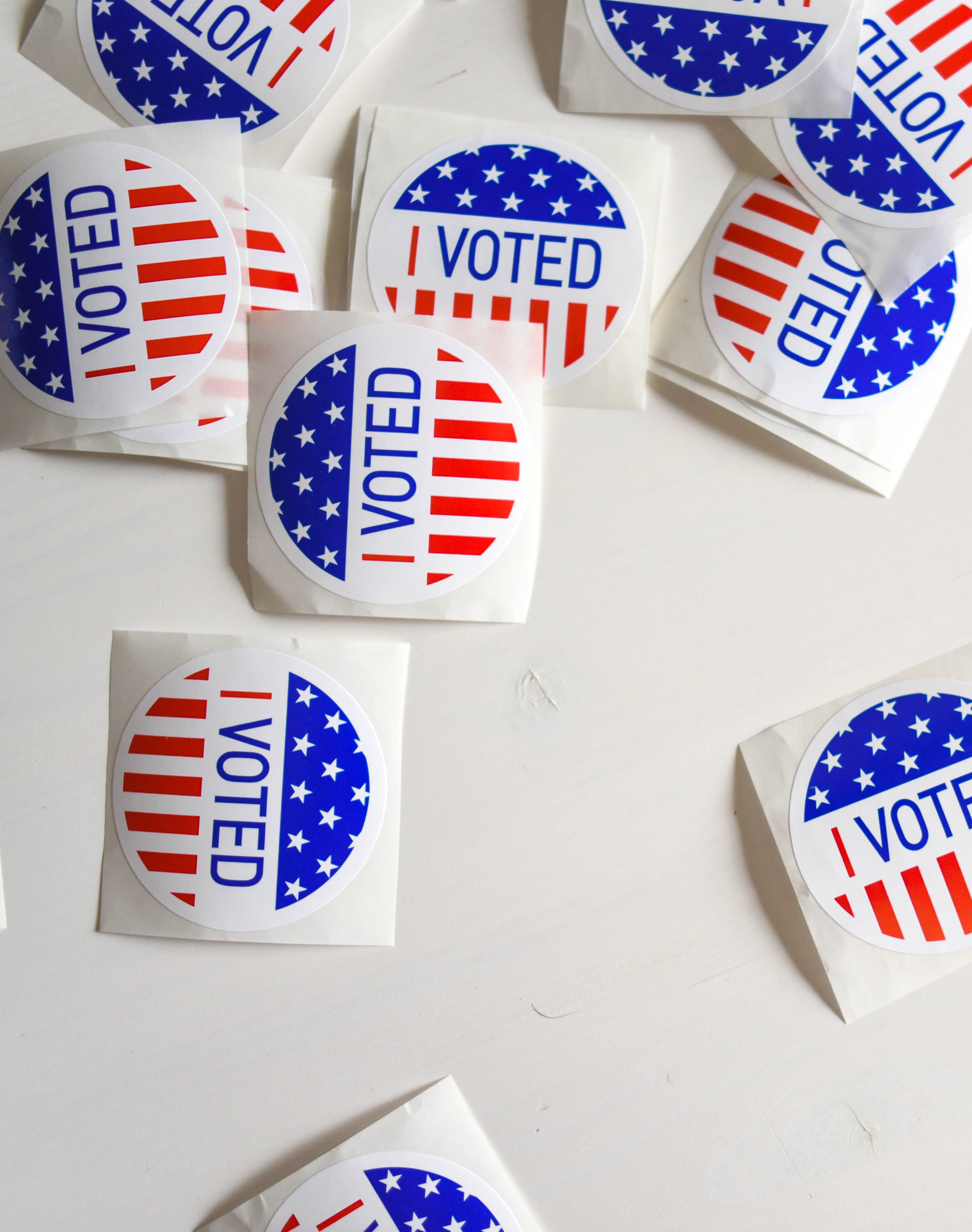 A bunch of red, white, and blue "I Voted" stickers are scattered across a white tabletop.