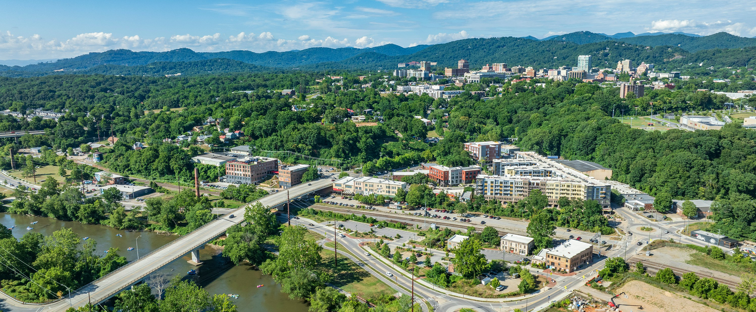 An aerial view of Asheville, with mountains behind and a river in the foreground.