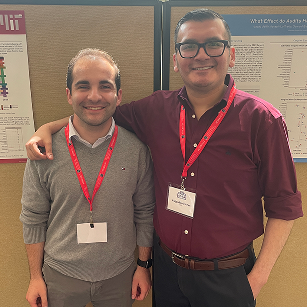 Two young men wrap an arm around each others' shoulders and grin in front of their posters at the 2023 ESRA conference.