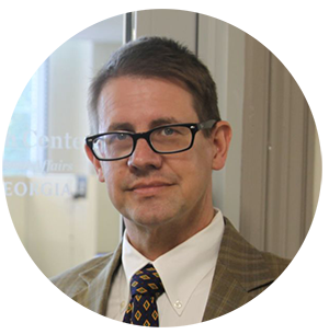 A white man with close cropped brown hair and glasses looks at the camera.