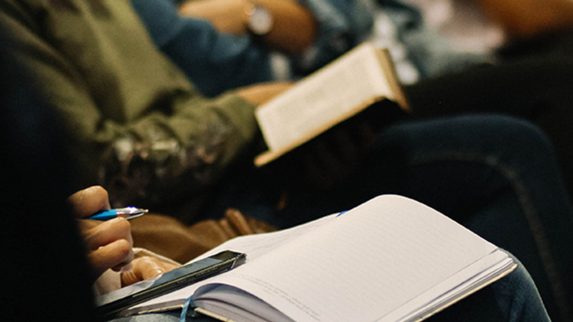 A woman balances her cellphone on top of an open notebook in a conference hall.