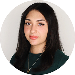 A young woman with long dark hair gives a slight smile to the camera. She is wearing a dark green shirt and a silver necklace.