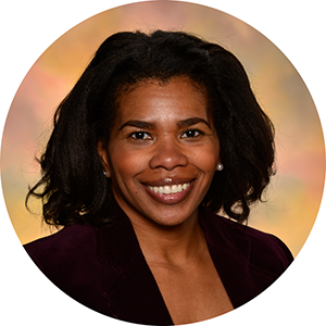 A Black woman gives the camera a wide smile. She has slightly wavy, chin-length hair, and is wearing a black suit jacket.